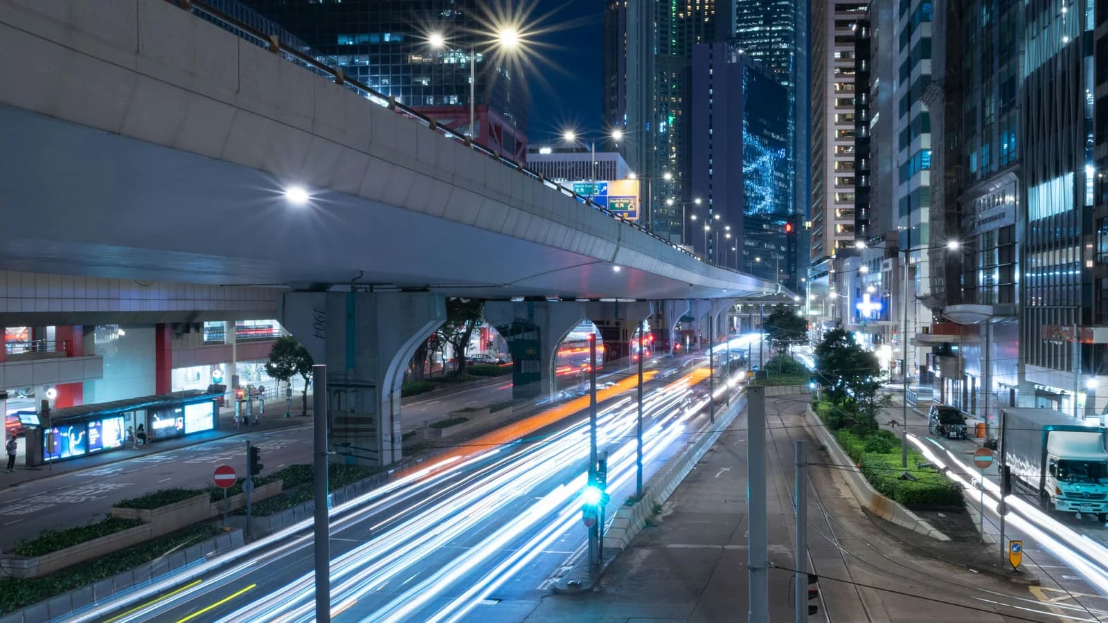 Long-exposure traffic trails move through a city street at night.